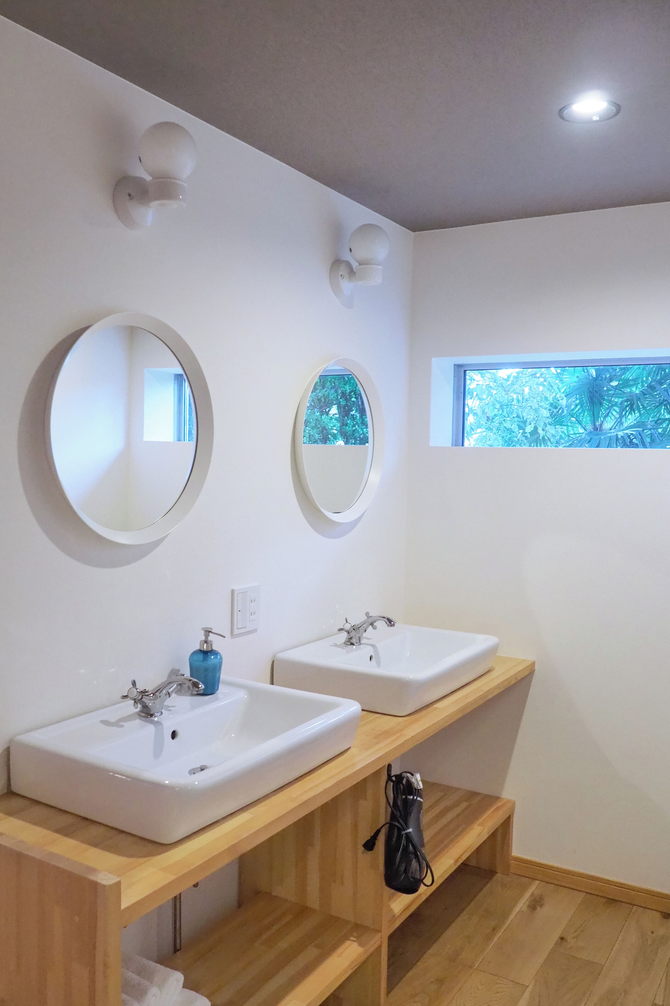 A bathroom with two sinks, round mirrors, and a window.