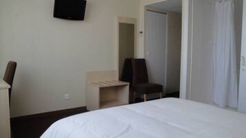 A hotel room with a bed, a desk, a chair, a television on the wall, and a door leading to another room.