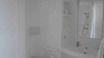 A bathroom with a toilet, a shower, and a sink with a mirror.