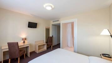 A hotel room with a bed, desk, chair, TV, and a door leading to another room.