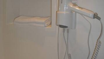 A bathroom with a hairdryer on a white wall, a towel rack, and a small bottle on the counter.