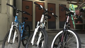 Tres bicicletas estacionadas en un área cubierta con techo, y tres puertas con la leyenda "Best Room" al fondo.