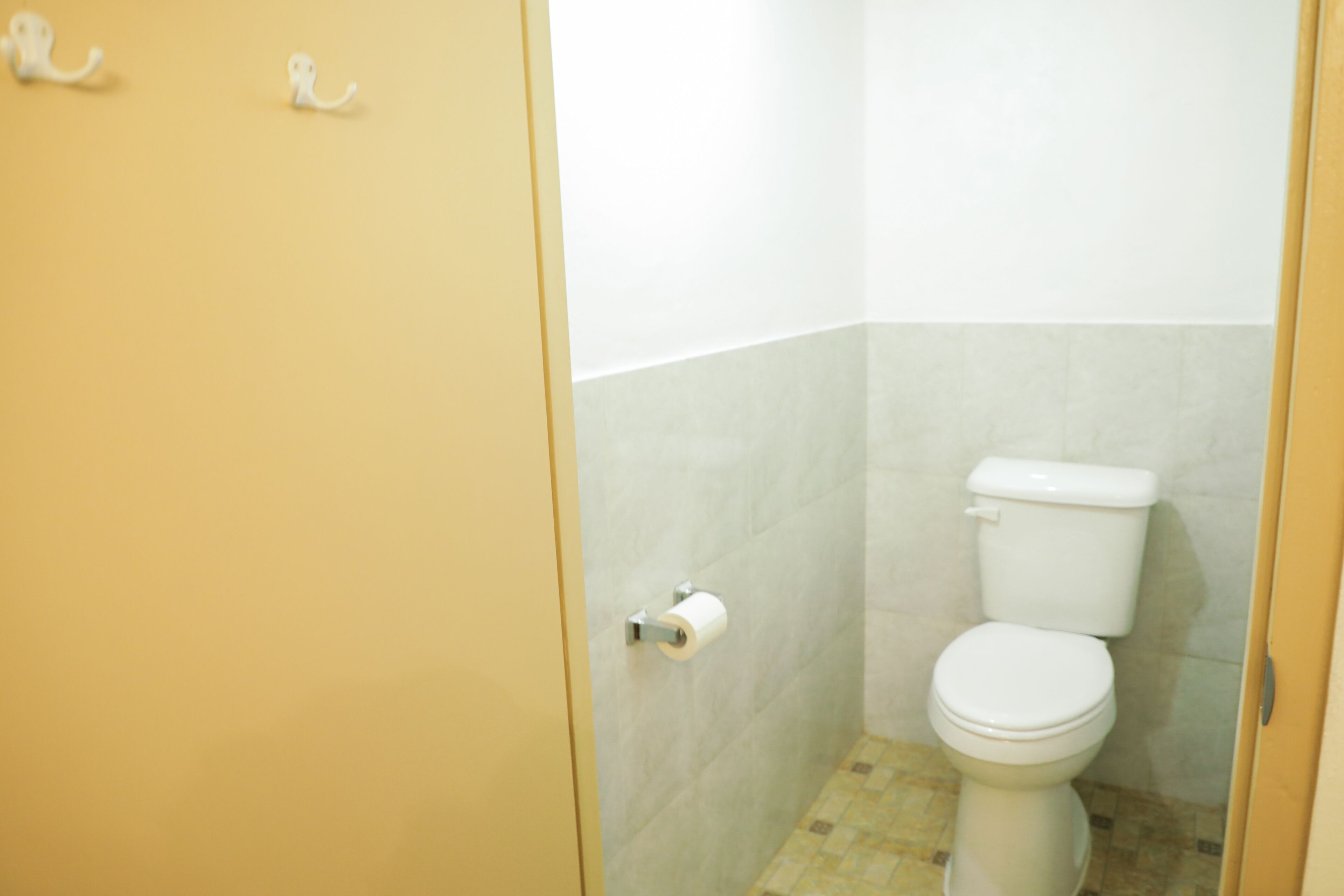 A small bathroom with a toilet, a roll of toilet paper on the wall, and a tiled floor.