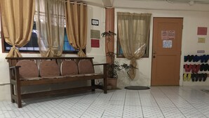 Una habitación con un banco de madera, una planta en maceta, suelo de baldosas y una puerta con zapateros.
