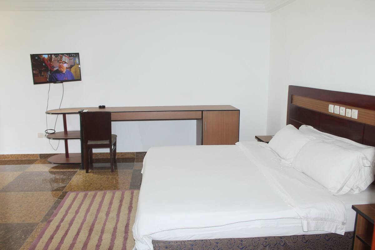 Una habitación de hotel con cama, escritorio, silla y televisión en la pared.