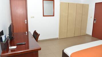 A hotel room with a wooden desk, a bed with an orange bedspread, a wardrobe, and a mirror on the wall.