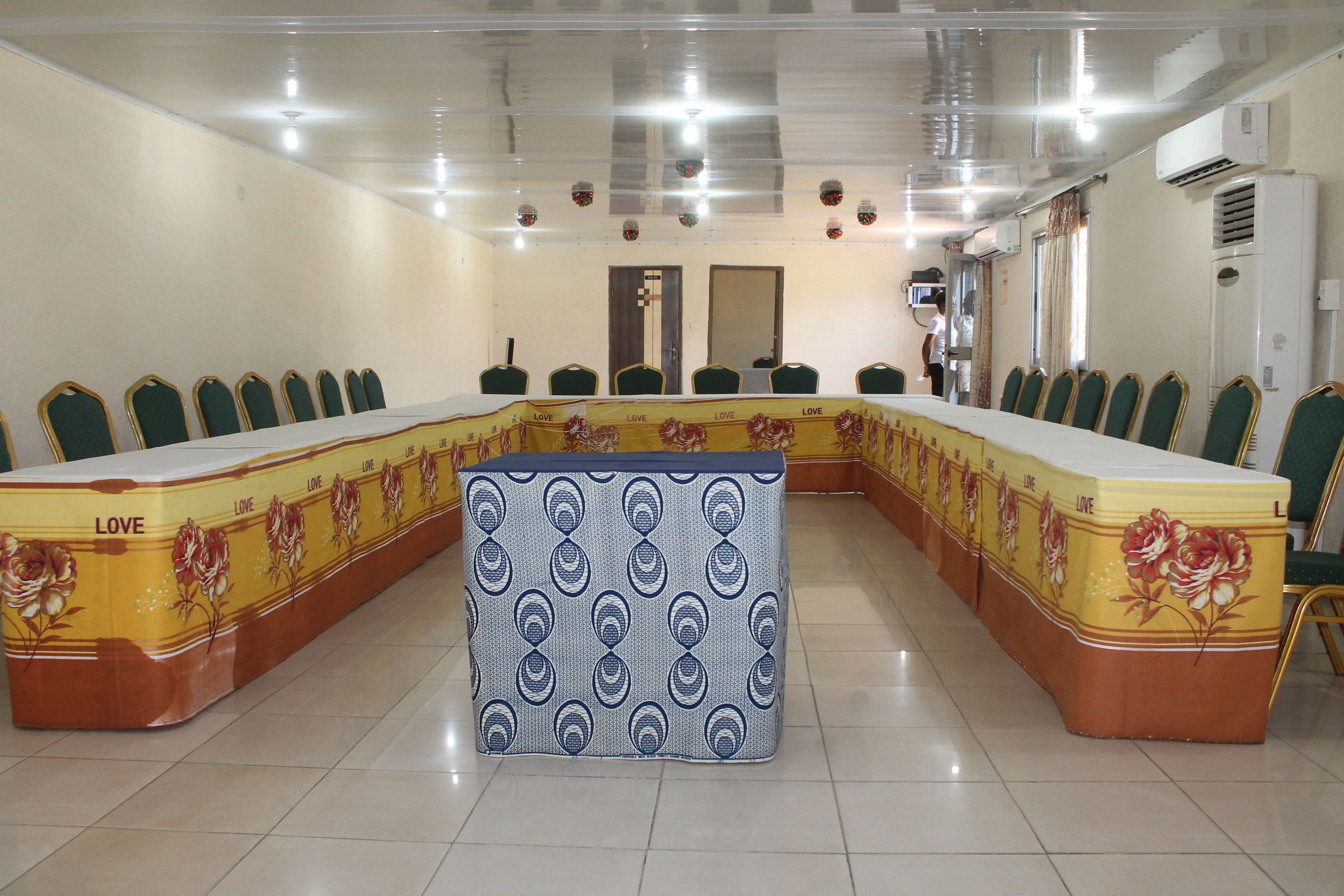 A conference room with a long table, green chairs, and a patterned tablecloth.