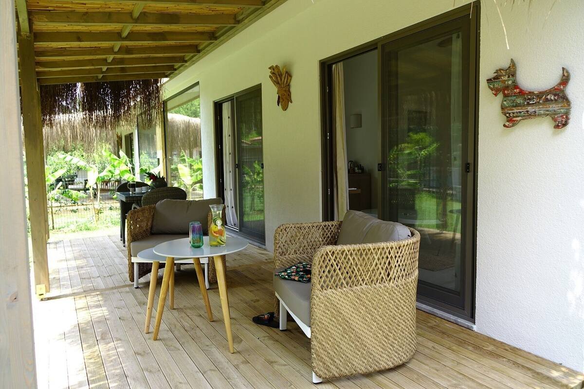 A covered outdoor seating area with wicker furniture, a small round table, and a glass pitcher.