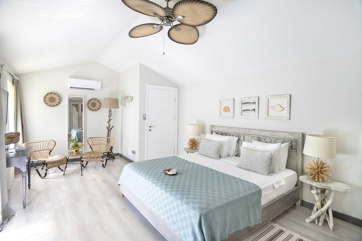 A bedroom with a bed, two chairs, a desk, and a ceiling fan.