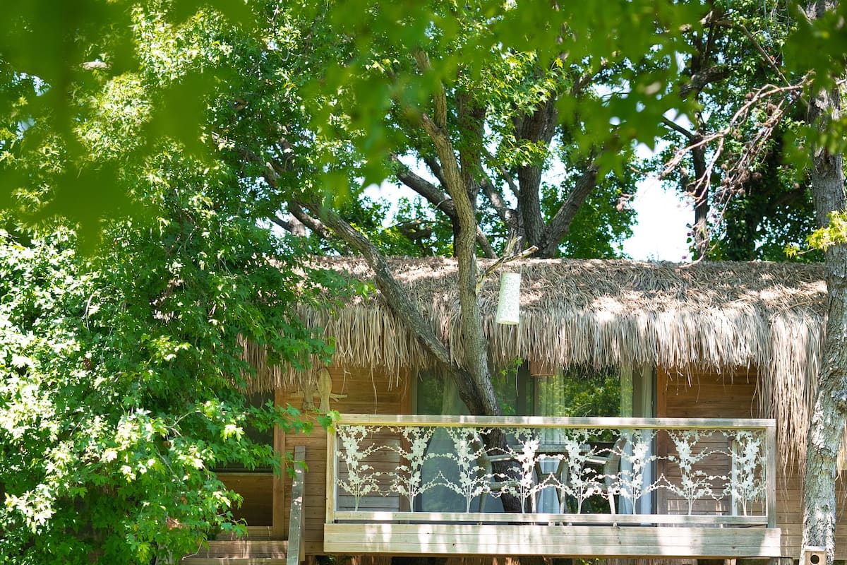 A treehouse with a thatched roof, a wooden staircase, and a balcony with a railing.