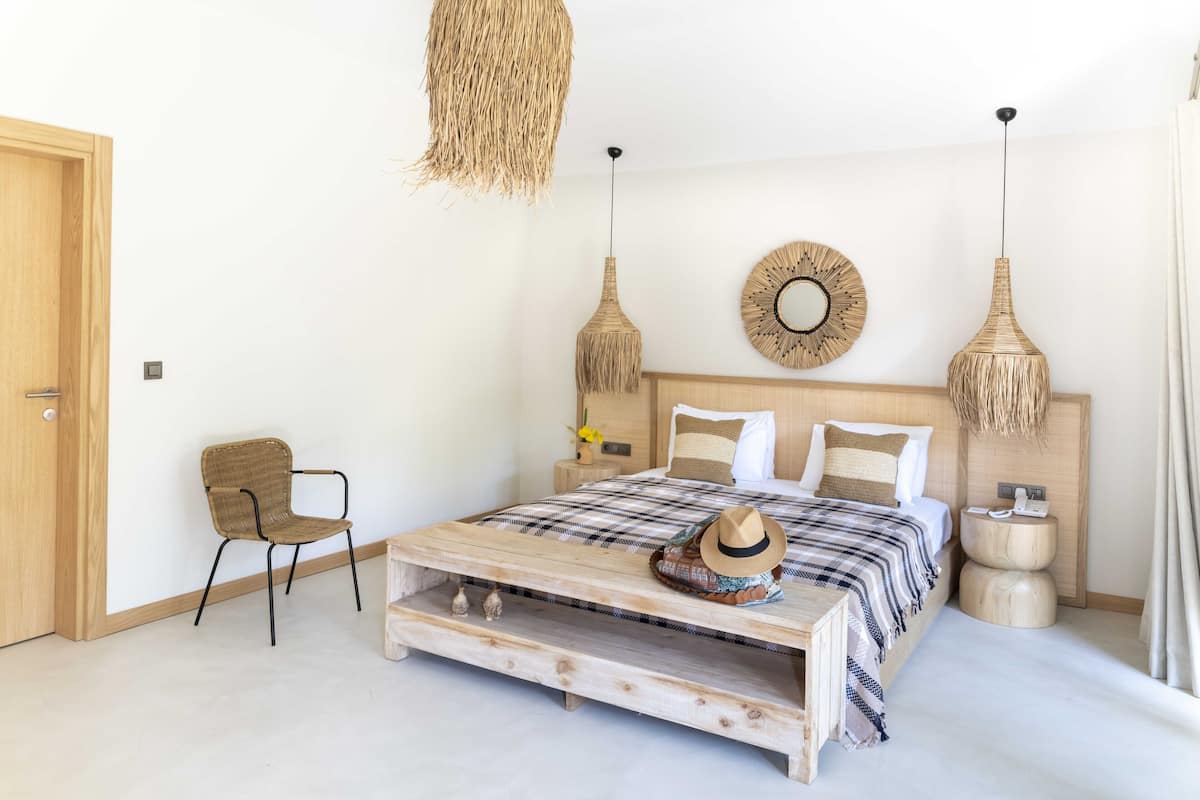 A bedroom with a wooden bed, a chair, a bedside table, and a hanging light fixture.