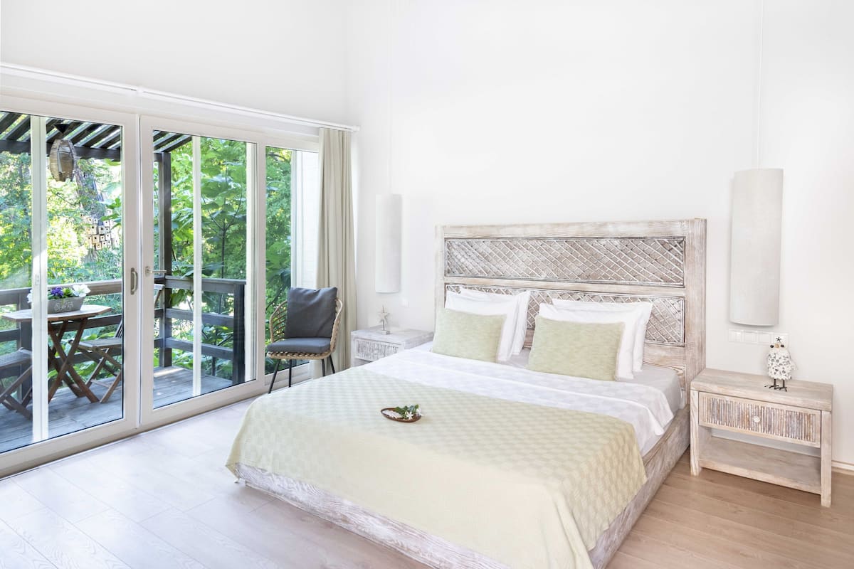 A bedroom with a large sliding glass door leading to an outdoor area, a bed with a wooden headboard, and a bedside table with a lamp.