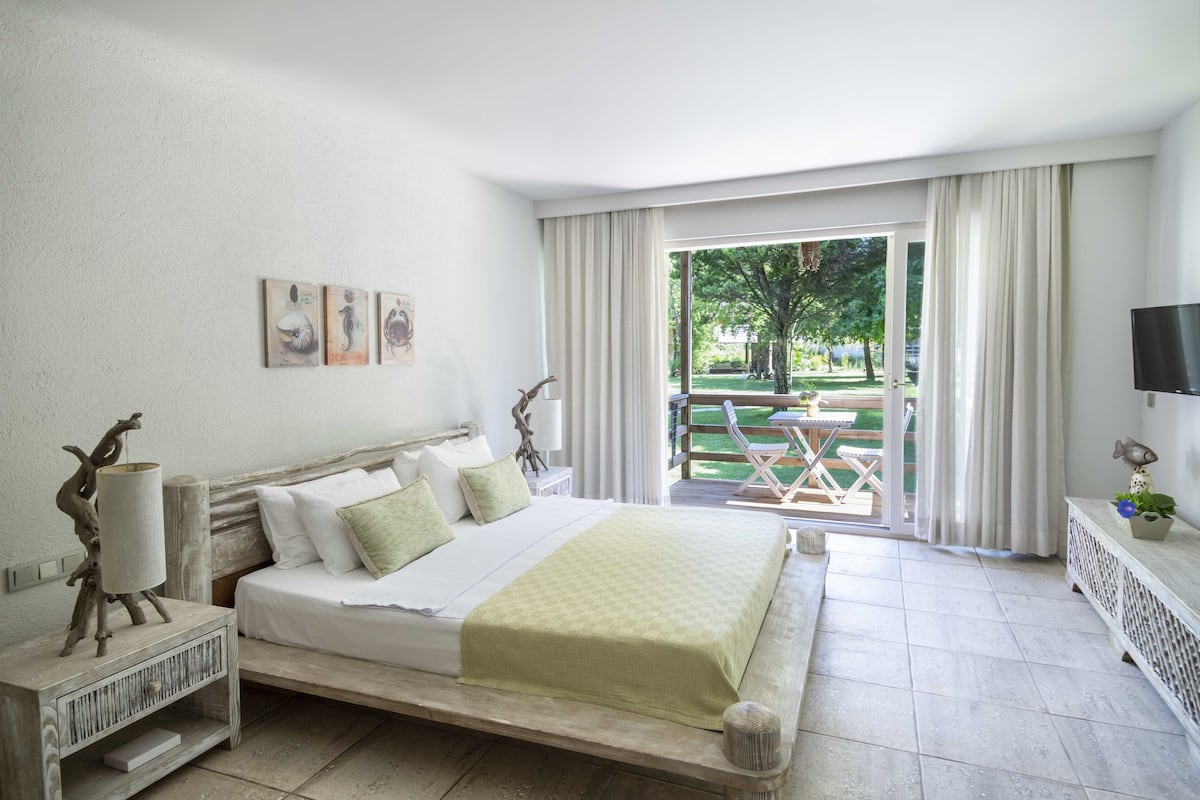 A bedroom with a bed, a nightstand, a TV, and a view of a garden through a sliding door.