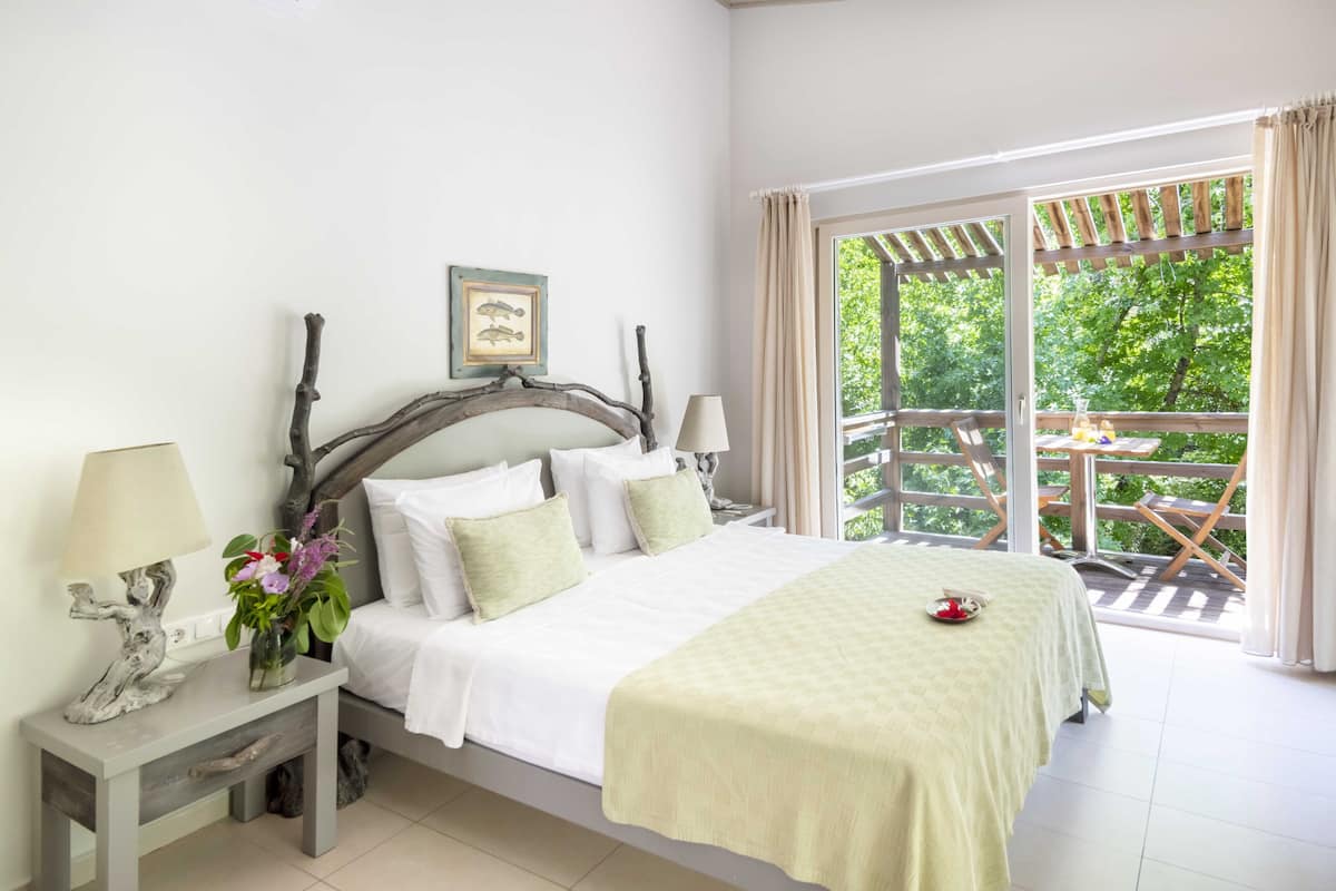 A bedroom with a bed, a nightstand, a lamp, and a view of a balcony with outdoor furniture.