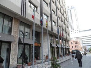Un hotel con fachada moderna, varias banderas y una zona de estacionamiento.