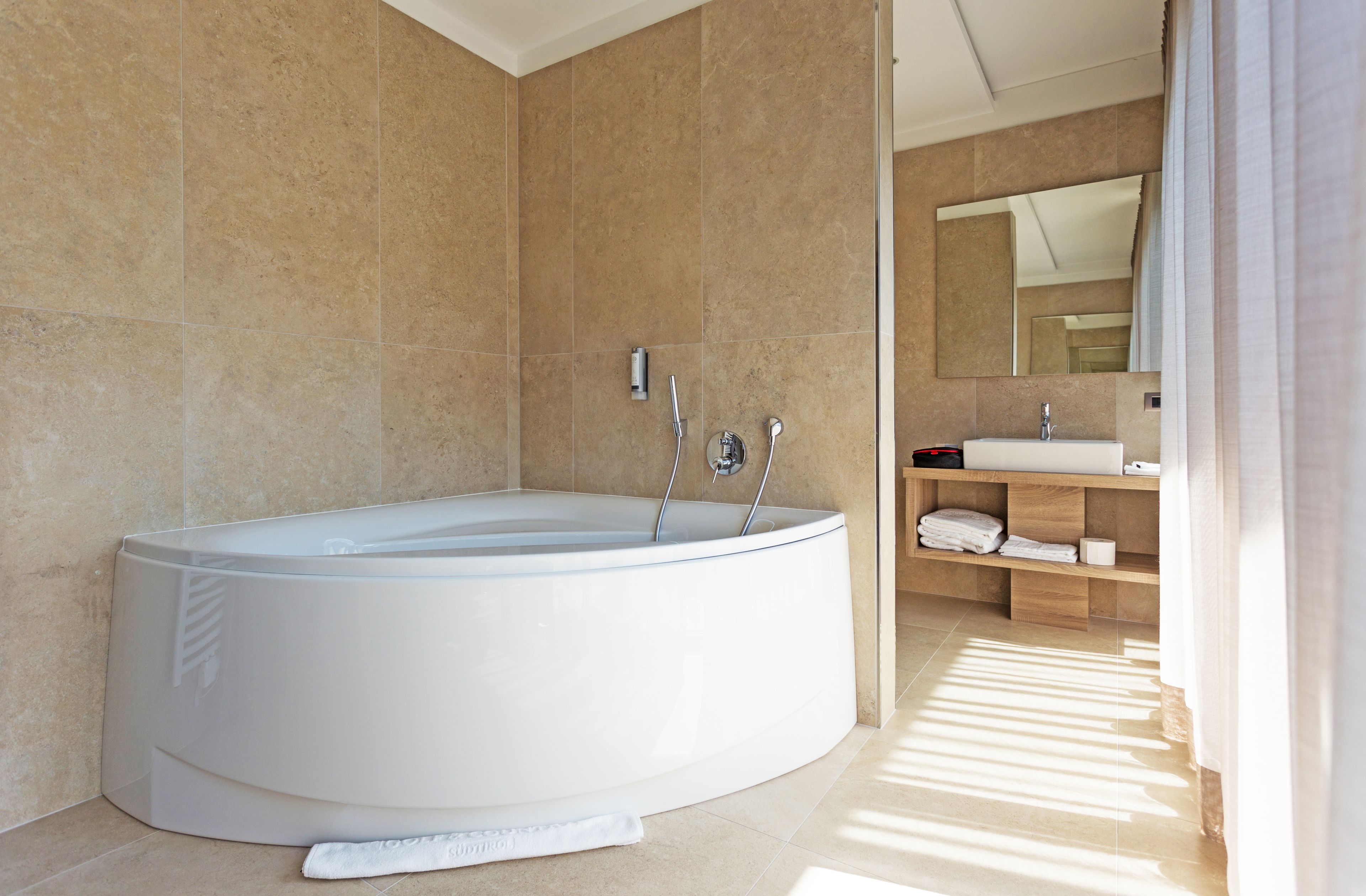 Une salle de bain moderne avec une grande baignoire sur pieds, un meuble-lavabo avec un miroir et une étagère en bois où sont posées des serviettes.