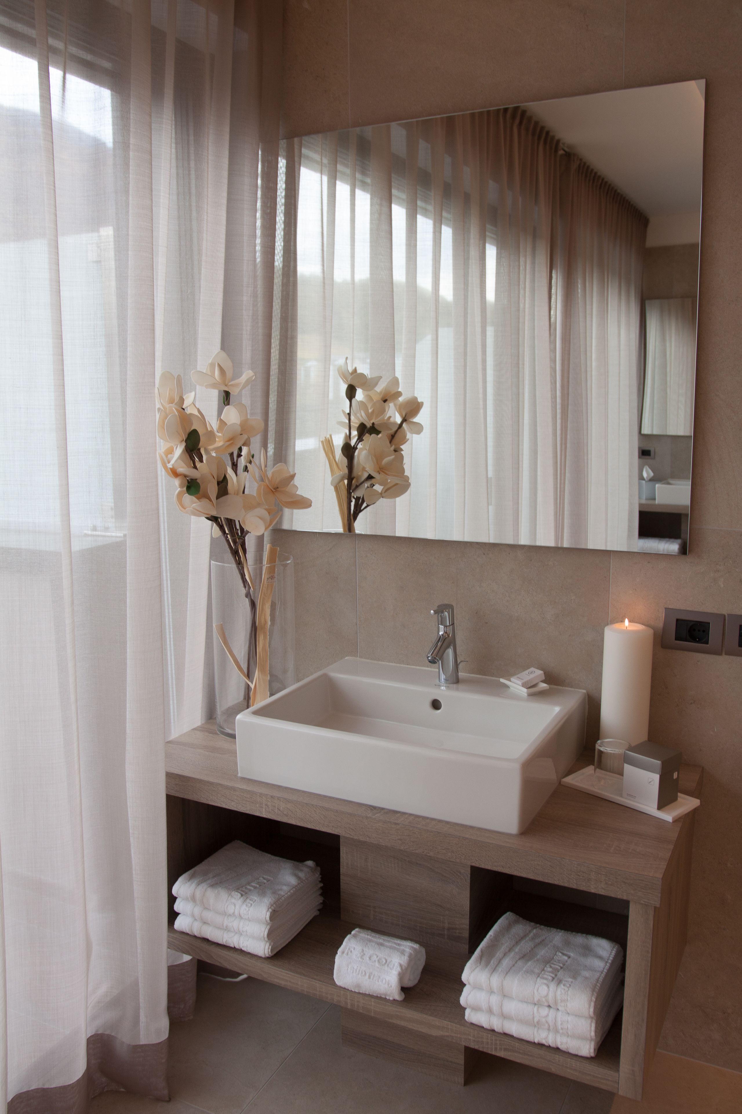 Une salle de bain moderne avec un grand miroir, un lavabo blanc et une étagère où sont pliées des serviettes.