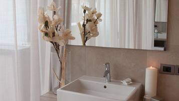 Une salle de bain moderne avec un grand miroir, un lavabo blanc et une étagère où sont pliées des serviettes.