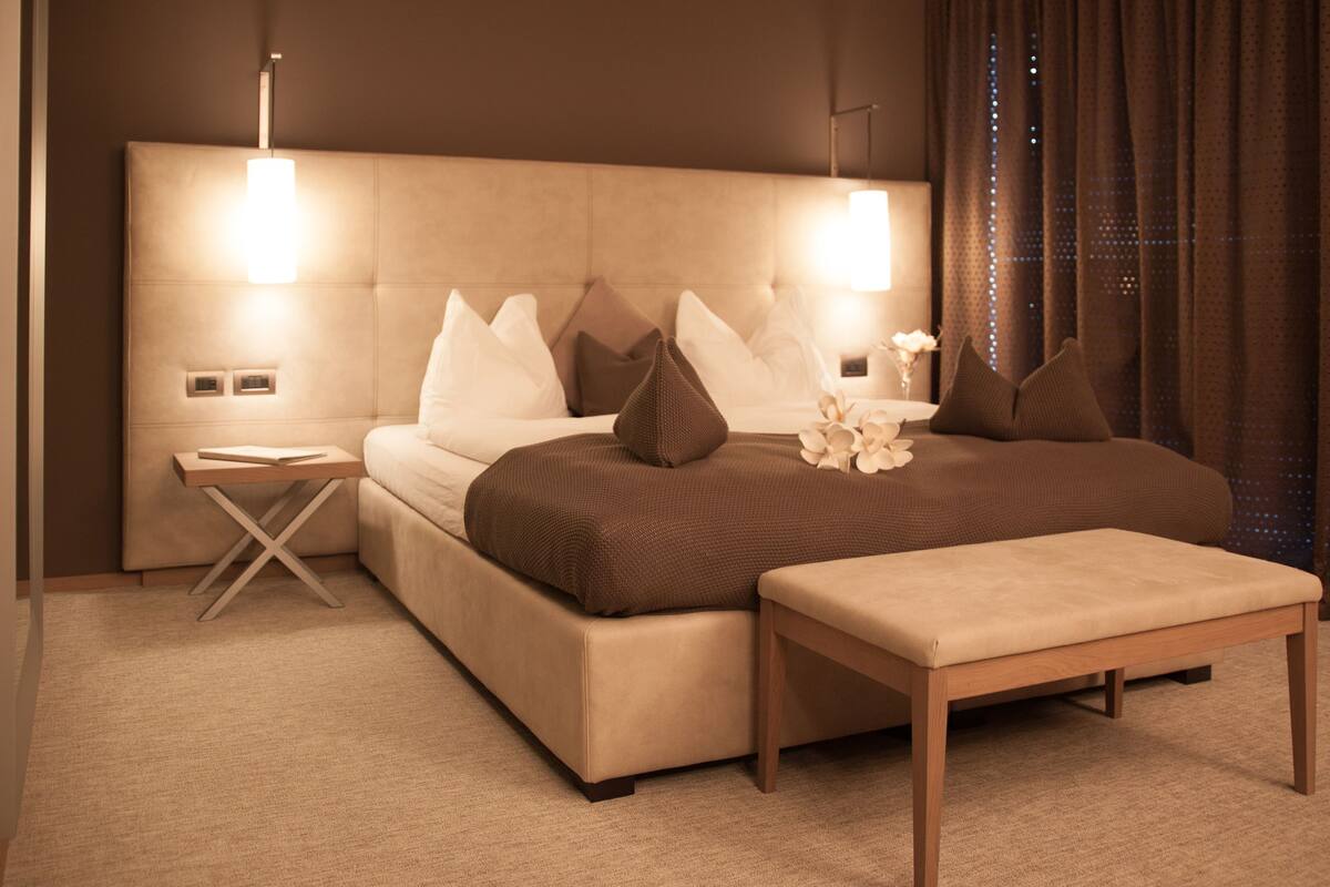 Ein modernes Schlafzimmer mit einem großen Bett, Nachttischen, einer Bank und einem Kopfteil mit integrierter Beleuchtung.