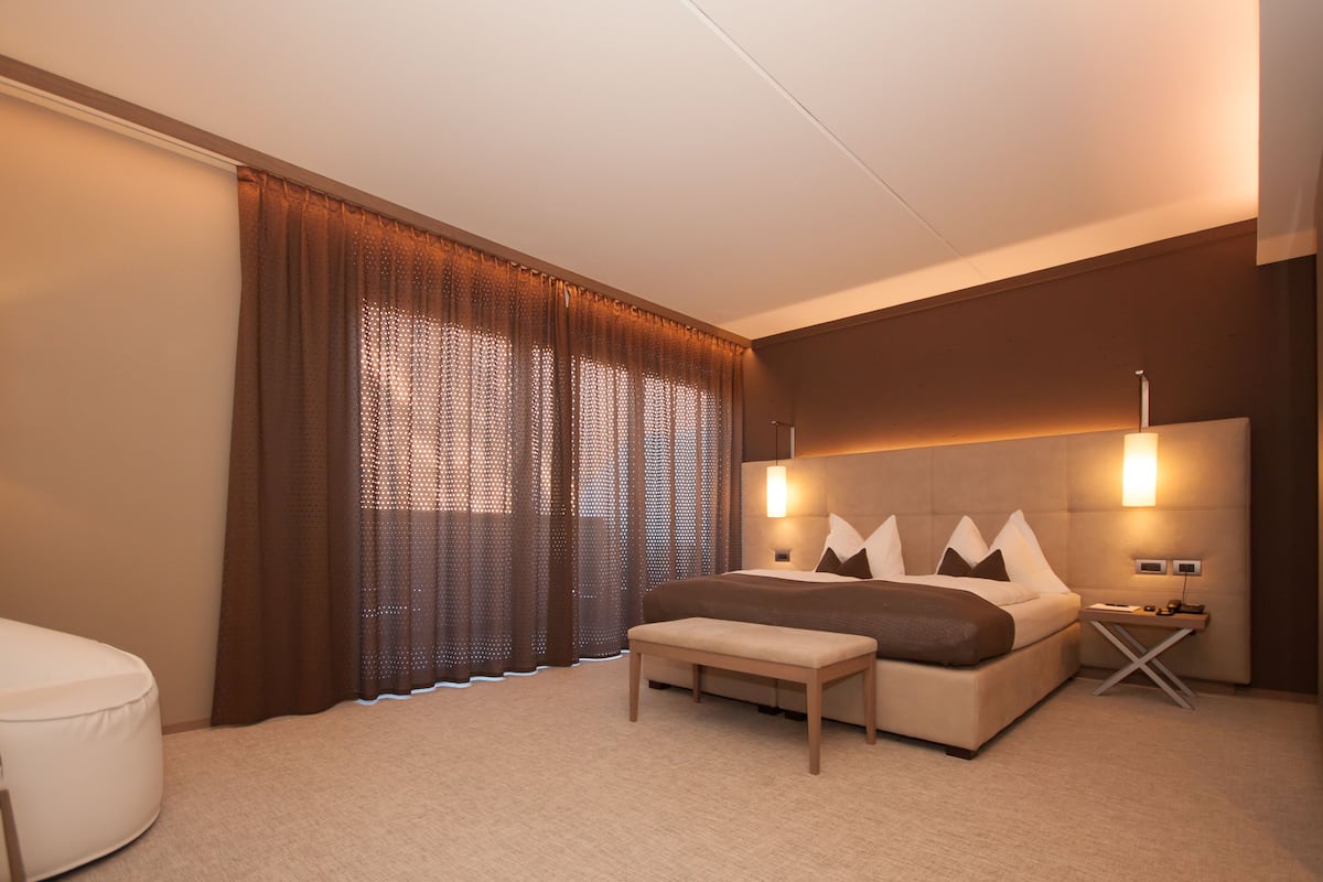 Ein modernes Hotelzimmer mit einem großen Bett, einem Nachttisch, einer Lampe und einem Fenster mit Vorhängen.