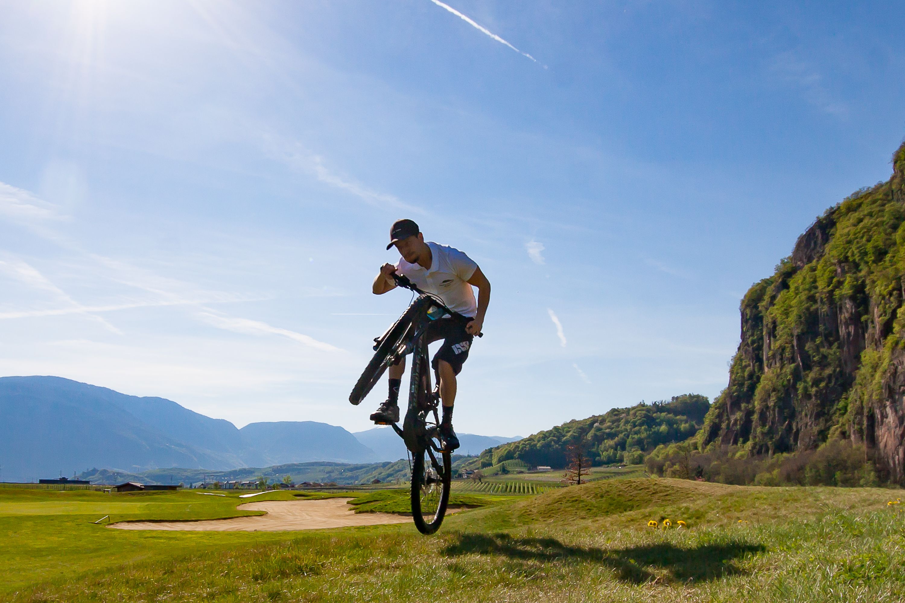 Eine Person auf einem Fahrrad in einem grünen Feld, im Hintergrund Berge.