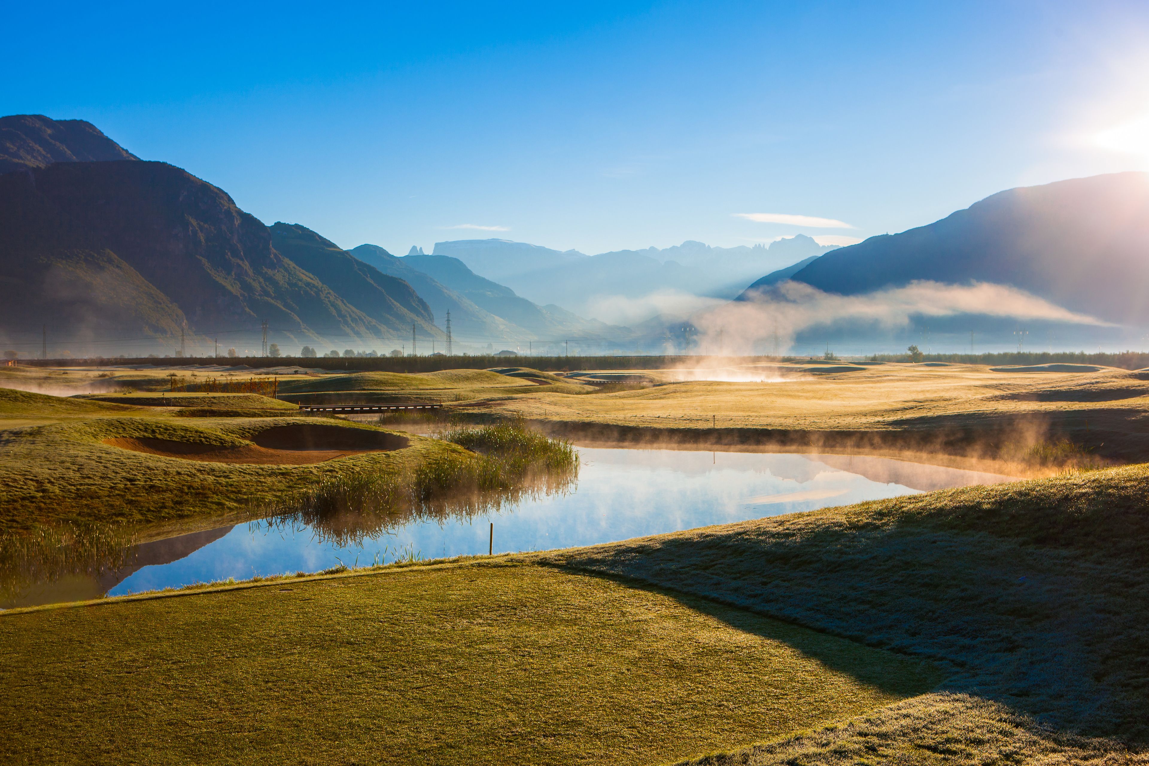 Paisagem serena com um lago tranquilo, colinas ondulantes e montanhas ao longe.