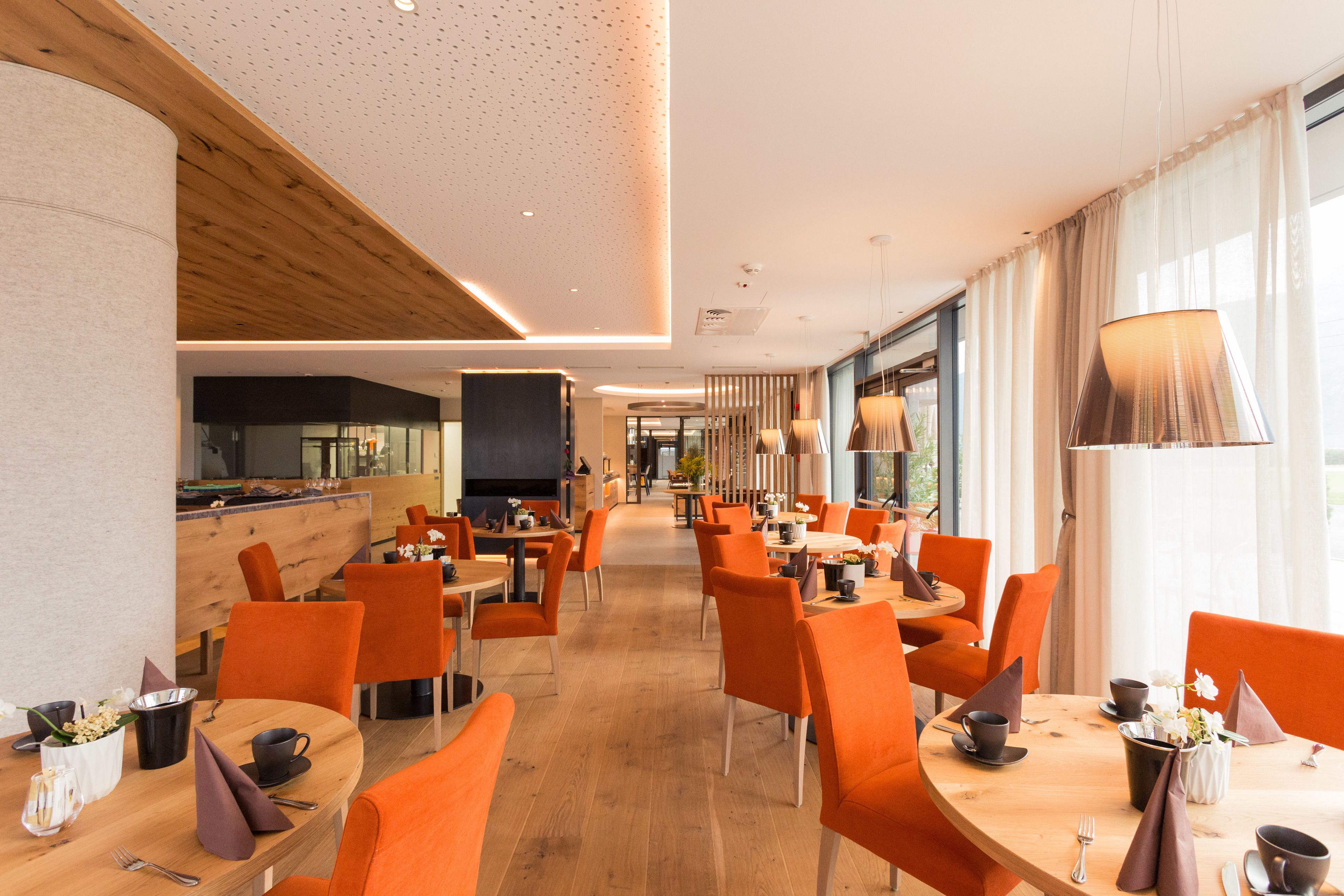 A modern dining area with orange chairs, wooden tables, and a large window providing natural light.
