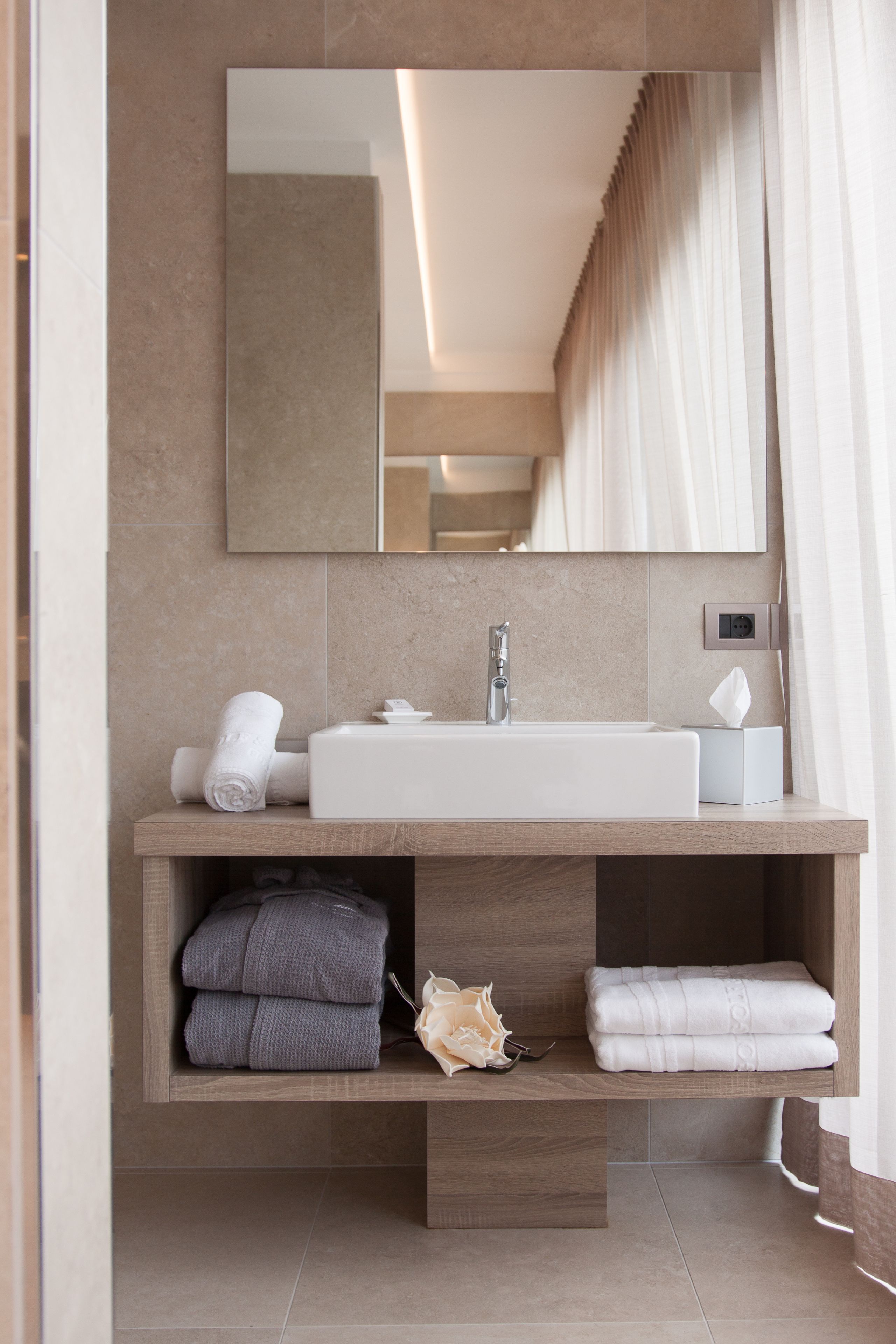 A modern bathroom with a large mirror, a sink, and a vanity with neatly folded towels and robes.