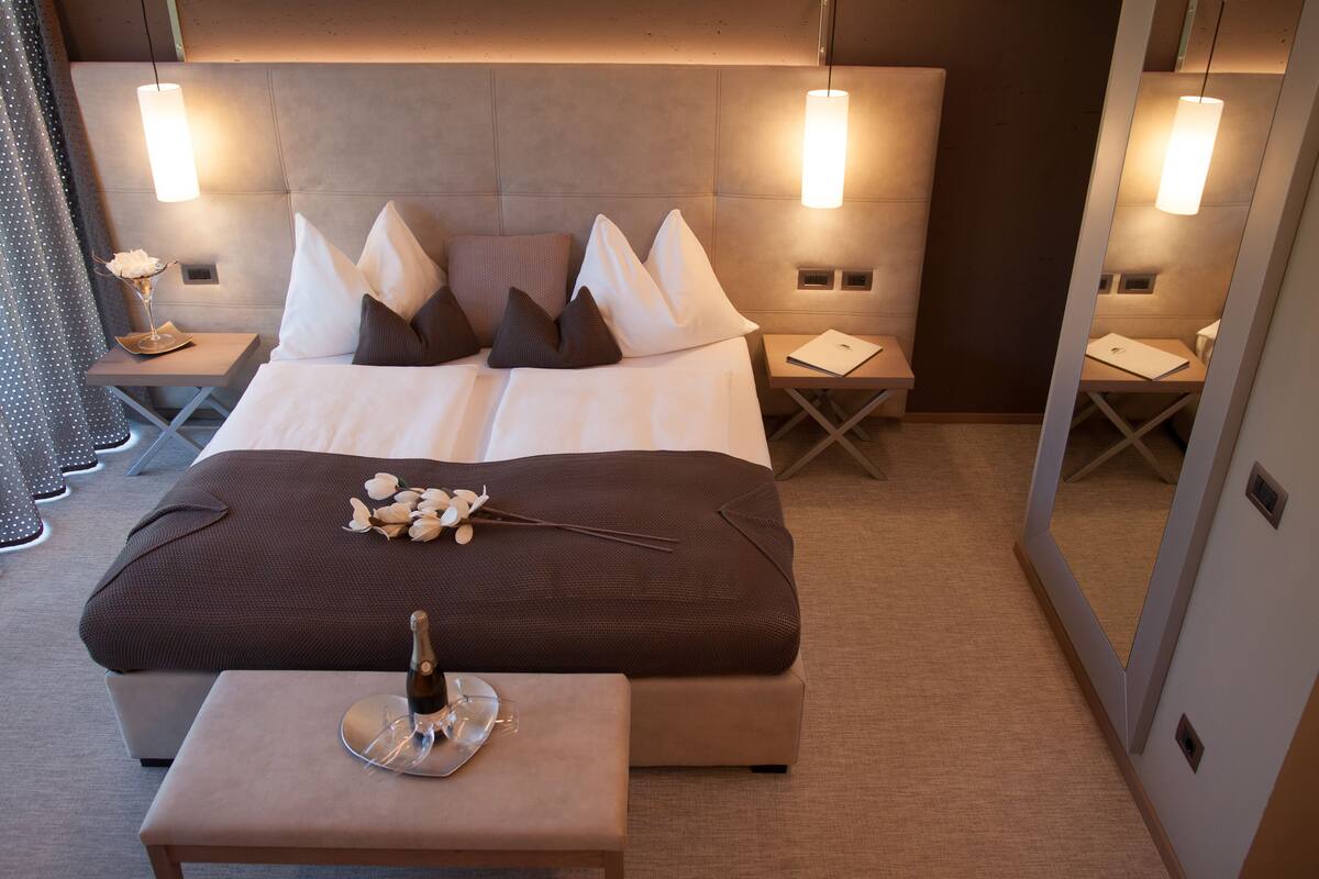 Ein modernes Hotelzimmer mit einem großen Bett, Nachttischen und einem kleinen Tisch mit Flasche und Gläsern.