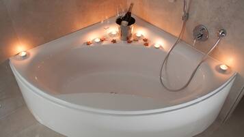 A large, oval-shaped bathtub with a champagne bottle and glasses, surrounded by candles.