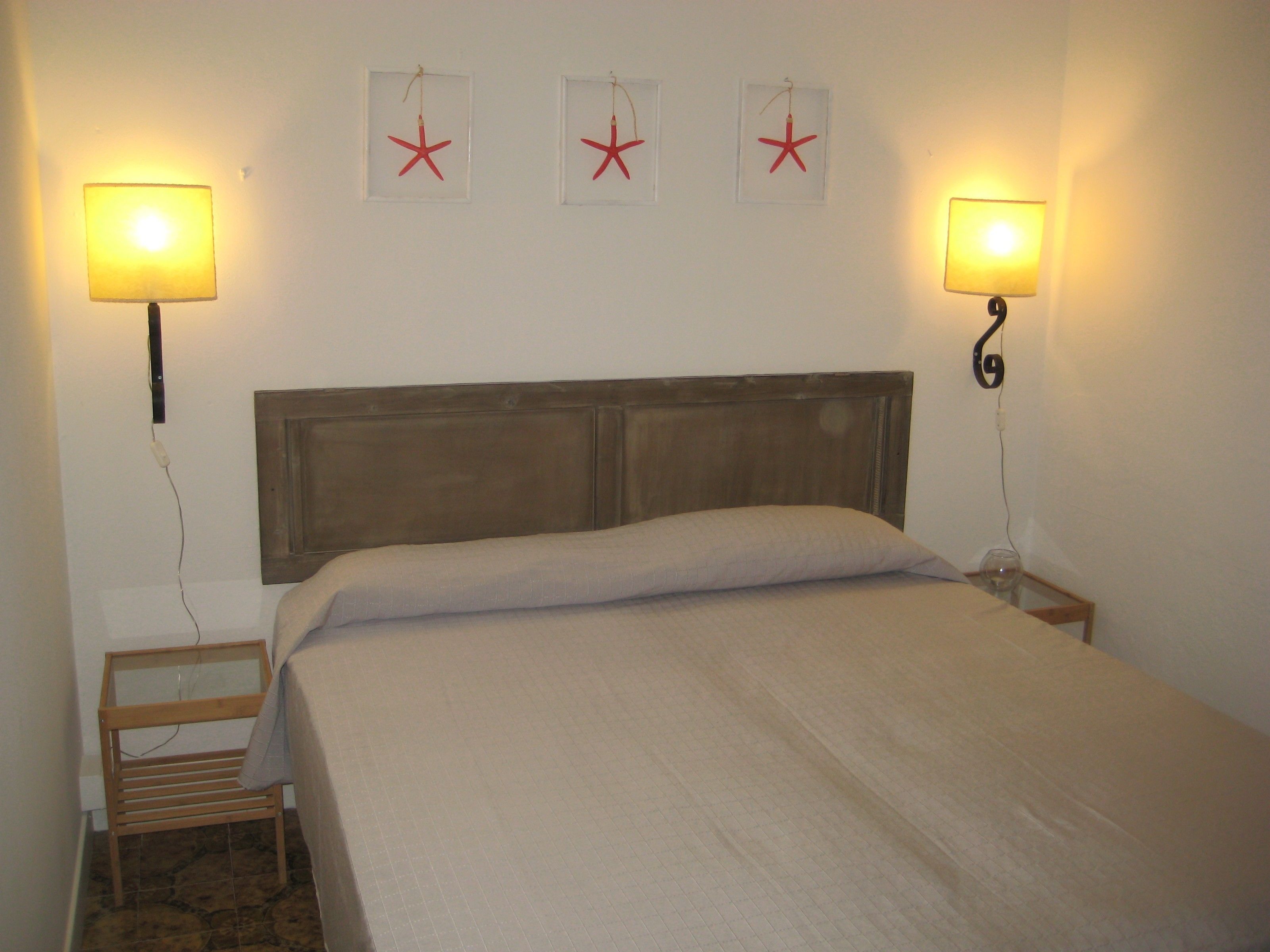 A neatly made bed with a wooden headboard, two bedside lamps, and three framed starfish decorations on the wall.