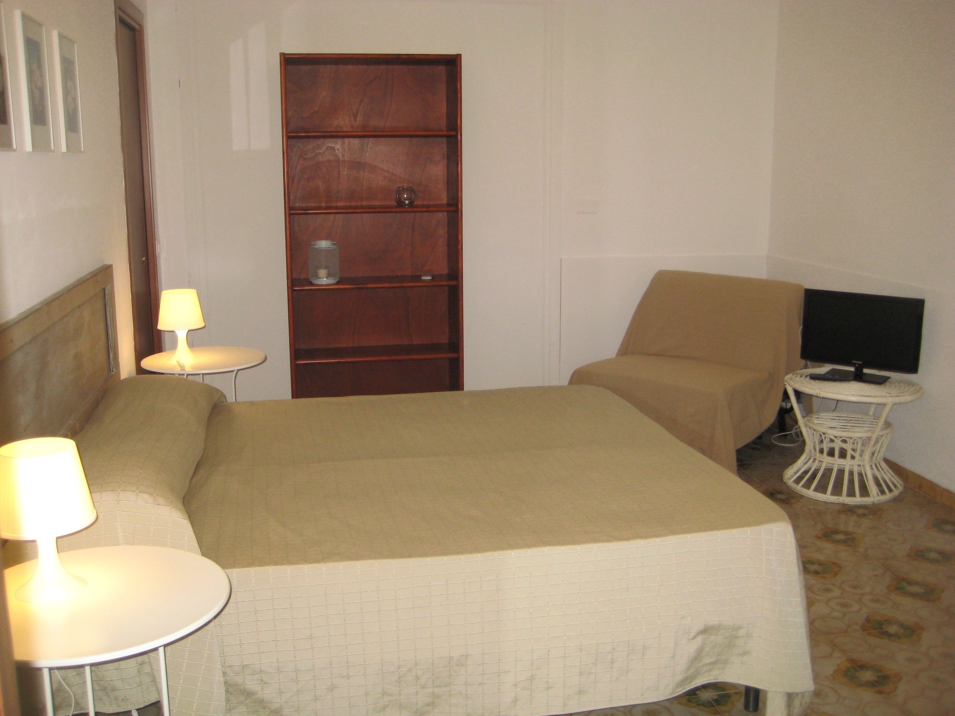 Une chambre d’hôtel avec un lit, deux tables de chevet avec des lampes, un téléviseur posé sur une petite table et une armoire en bois.