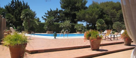 A pool area with tiled flooring, lounge chairs, and potted plants.