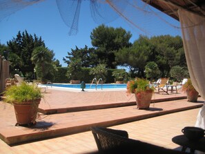 A pool area with tiled flooring, lounge chairs, and potted plants.