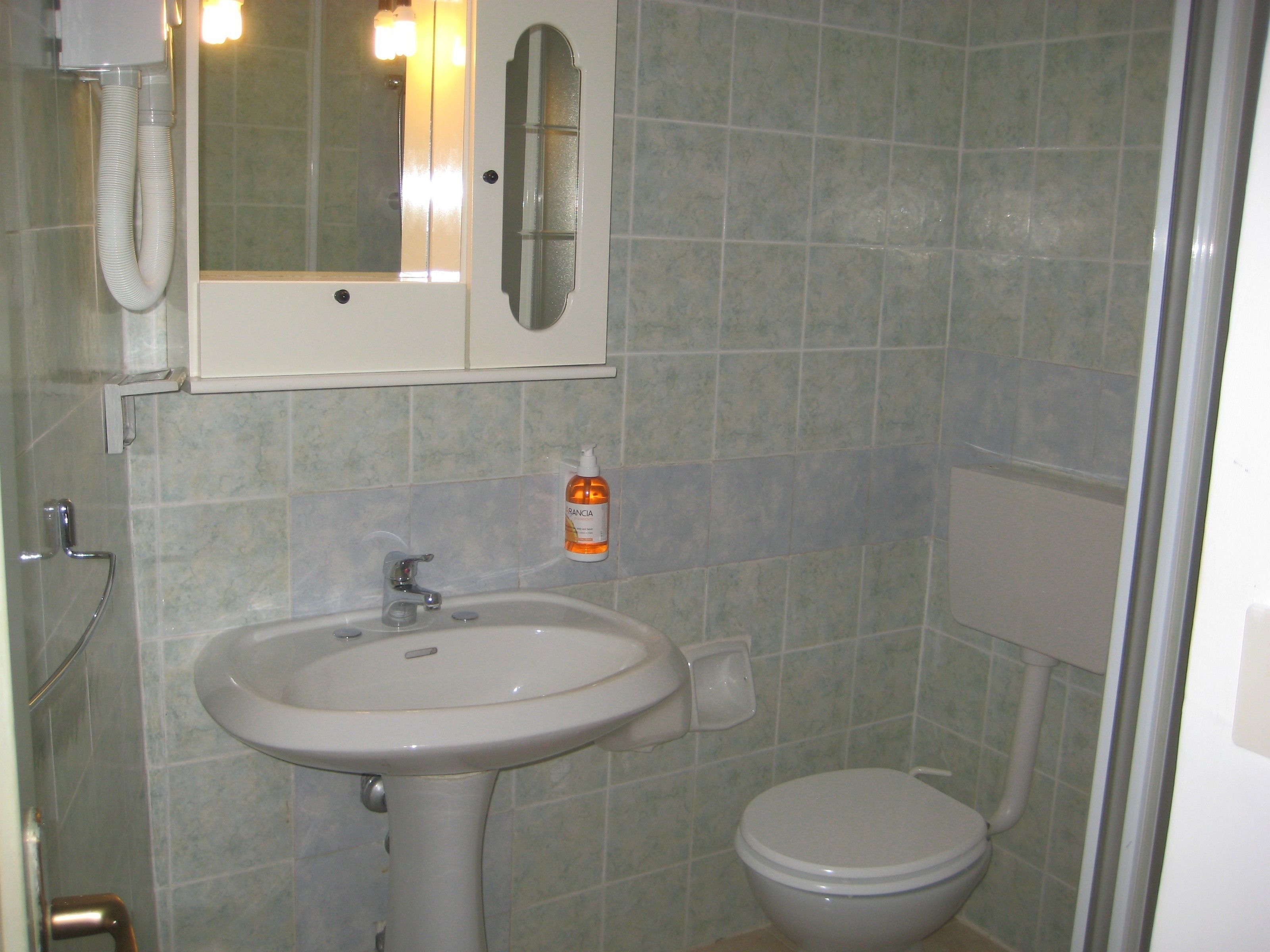 A bathroom with a sink, mirror, toilet, and a hand dryer.