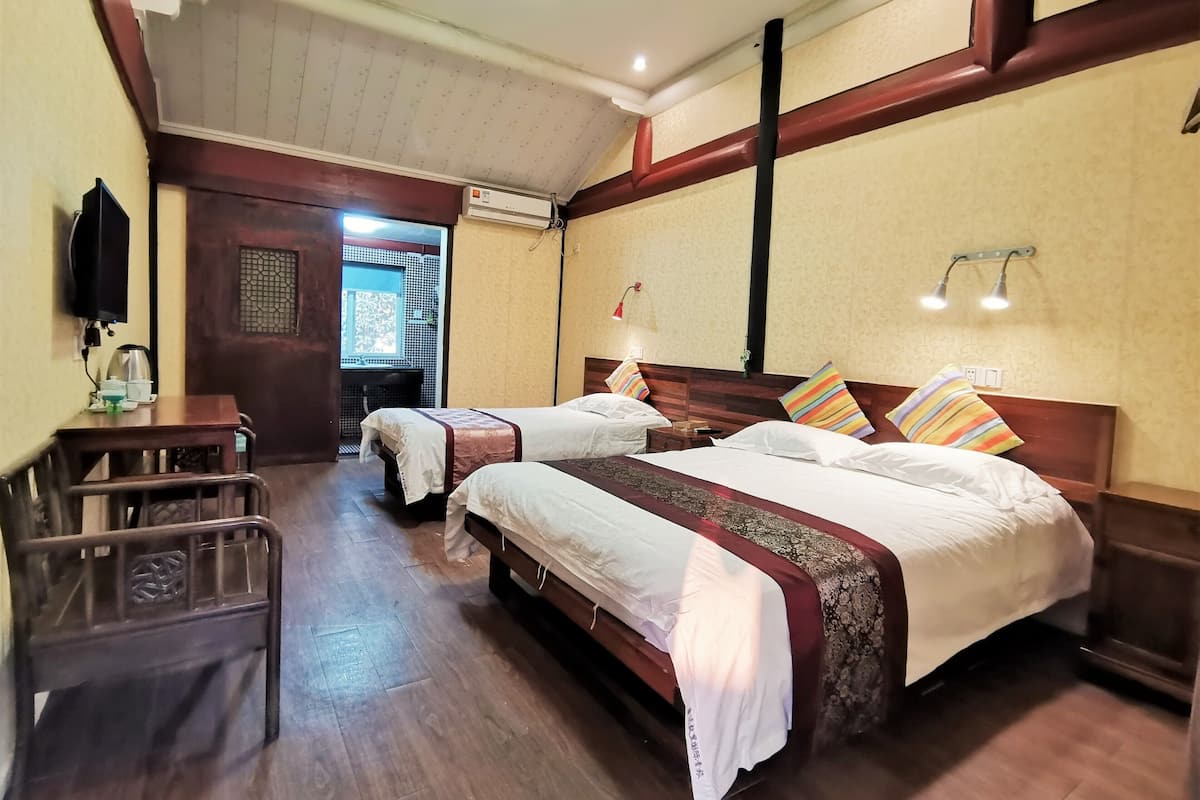 A hotel room with two beds, a desk, a chair, and a bathroom visible through an open door.