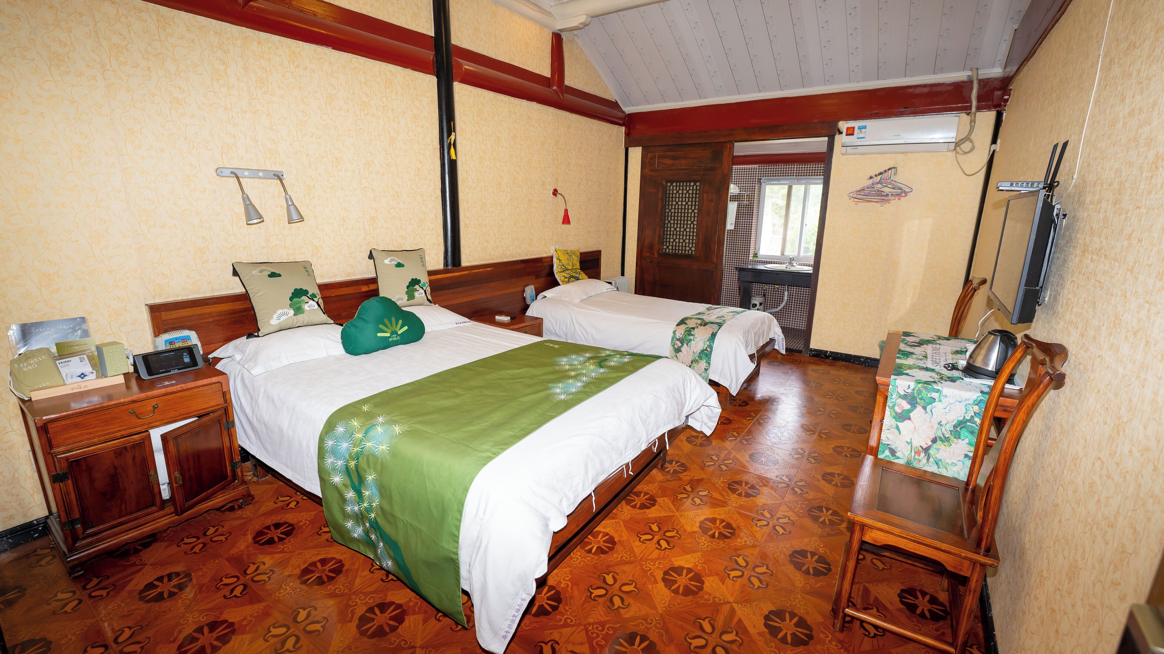 Habitación de hotel con dos camas, suelo de madera, escritorio con silla, espejo y ventana.