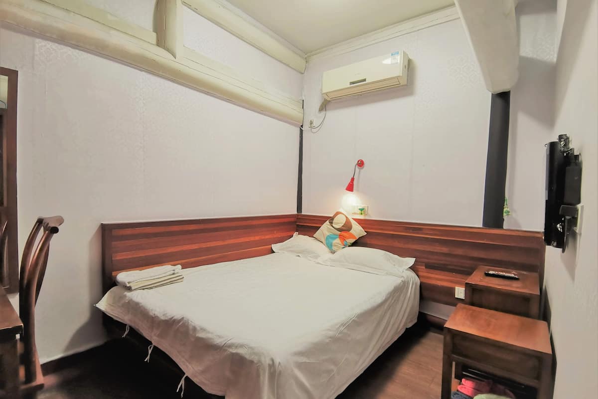 A hotel room with a bed, a nightstand, a lamp, an air conditioner, and a trash bin.