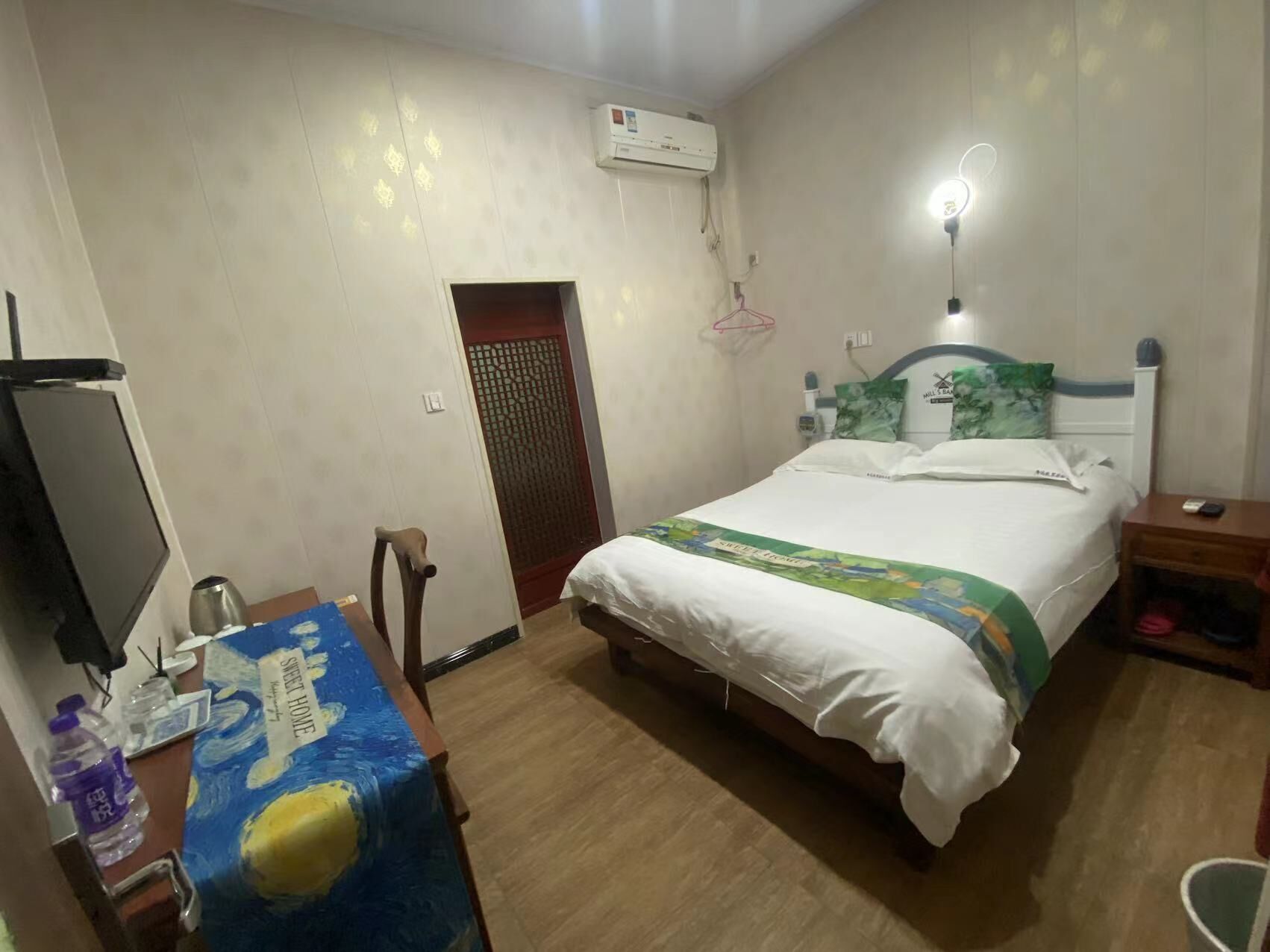 Quarto com cama, escrivaninha com computador, cadeira, ar condicionado e porta.