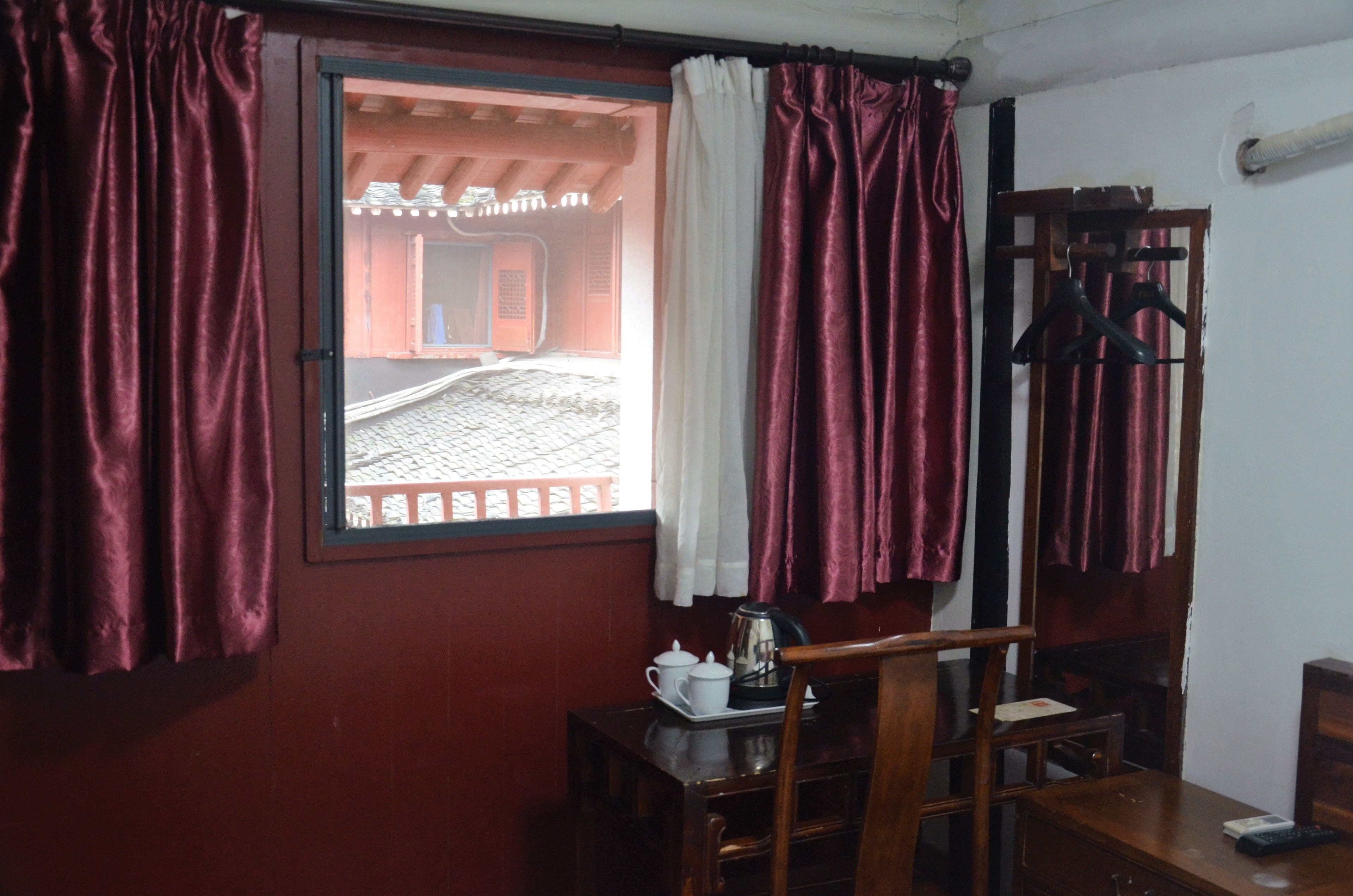 Una habitación con ventana, una mesa de madera, una silla, un perchero y un estante fijado a la pared.