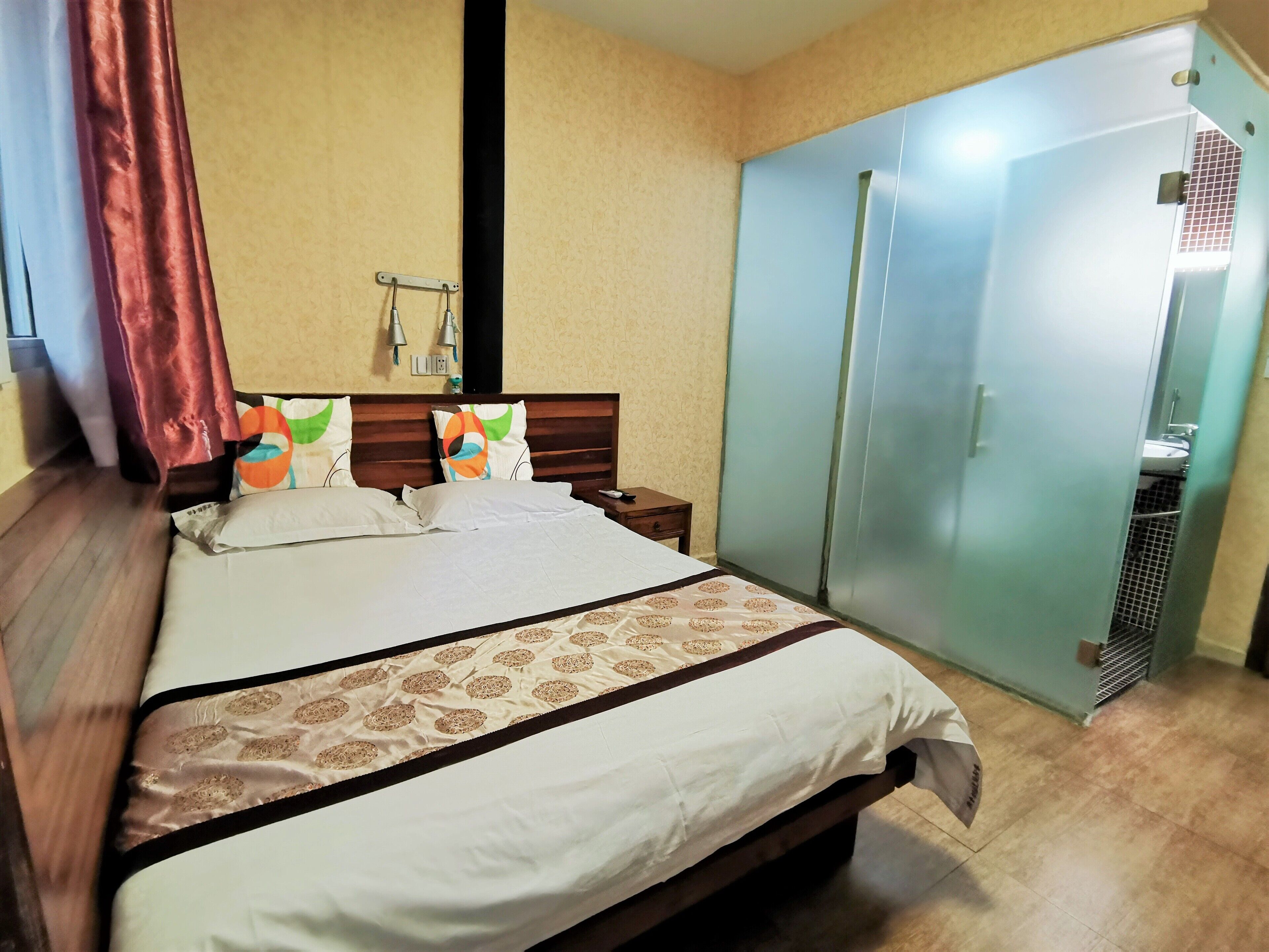 A hotel room with a bed, a wardrobe, a nightstand, and a wall-mounted light fixture.