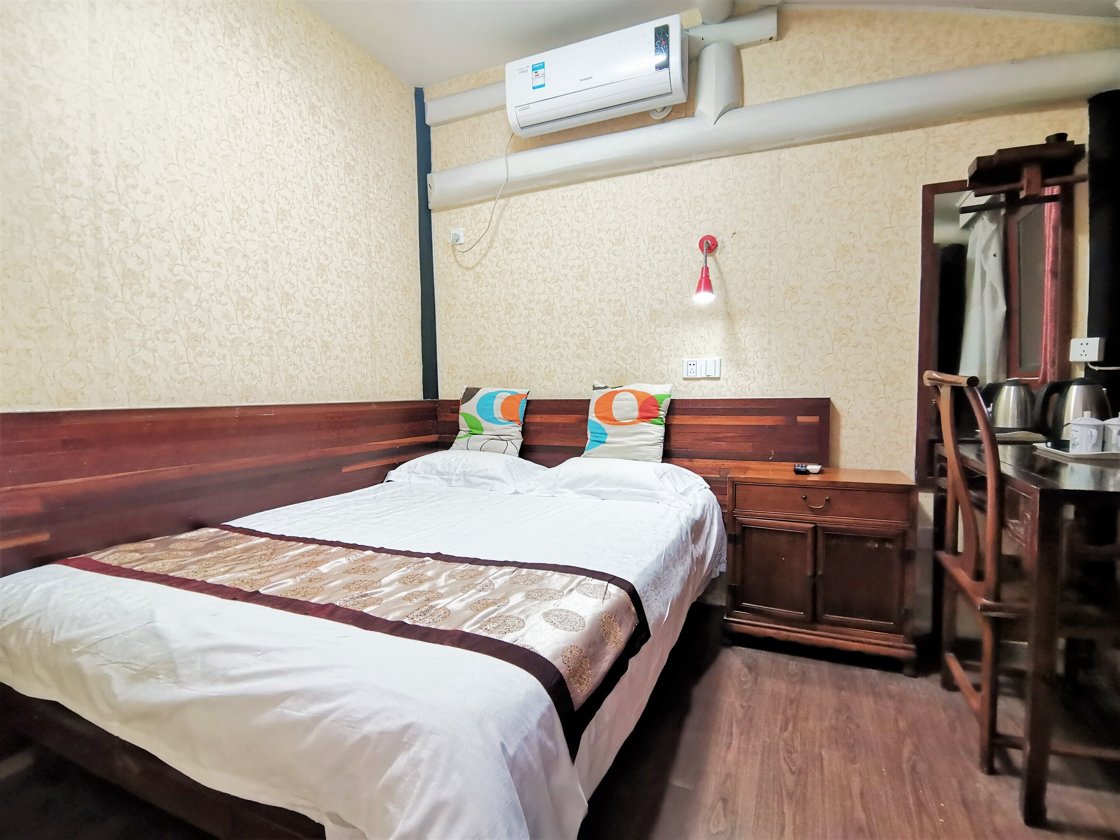 Habitación de hotel con una cama de madera, una mesita de noche, un espejo y un aire acondicionado instalado en la pared.
