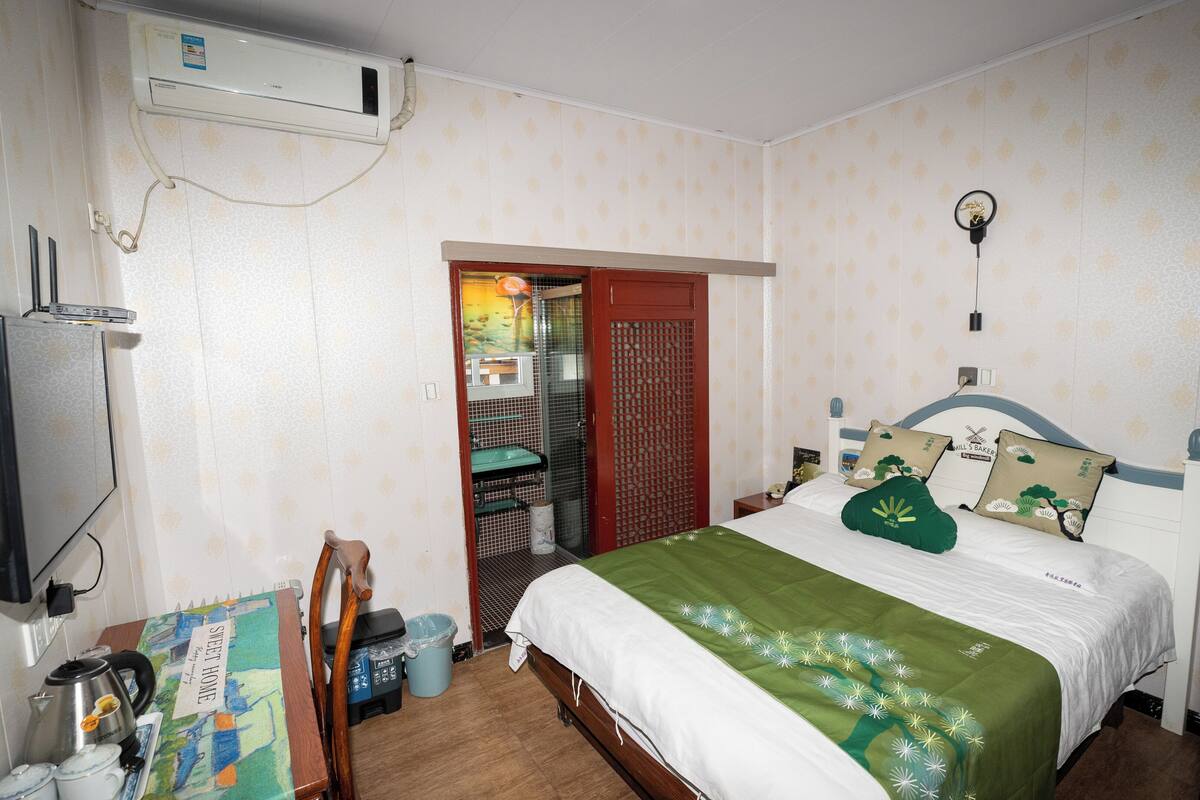 A bedroom with a bed, a TV, a heater, a window, and a door leading to a bathroom.