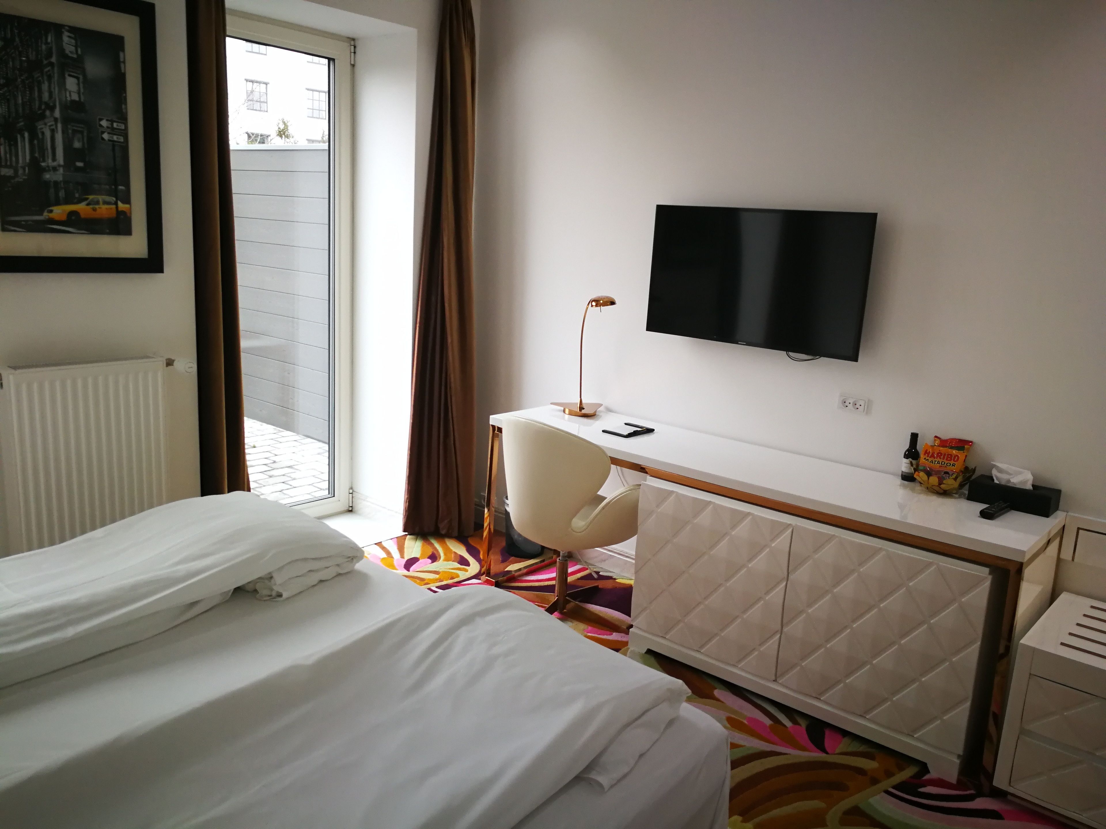 Habitación de hotel con cama, escritorio, silla, televisor y ventana con cortinas.