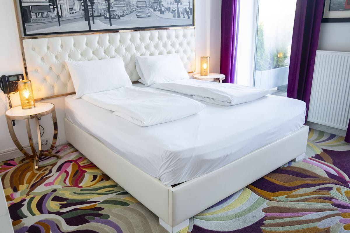 A neatly made bed with white linens, a tufted headboard, and two bedside tables with lamps.