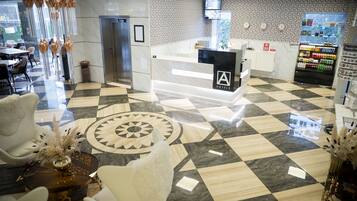 Un vestíbulo de hotel con mostrador de recepción, área de espera y mesas y sillas.