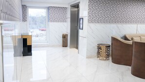 A modern lobby with a marble floor, a glass partition, a wooden trash bin, and a brown leather sofa. - A Hotels Glostrup (Brondby)