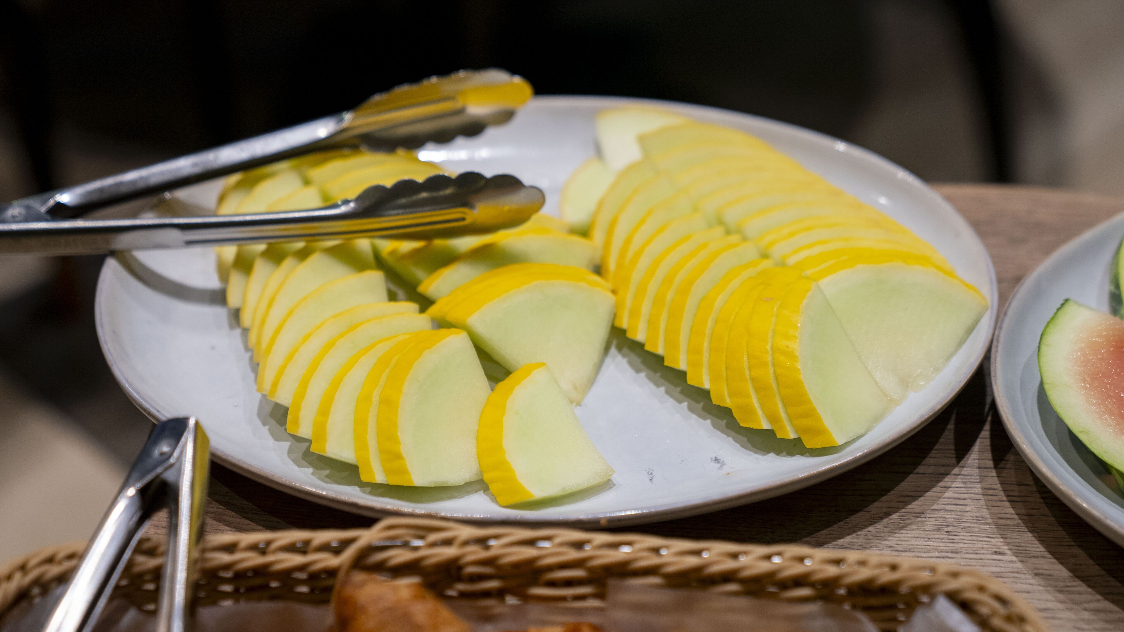 Ein Teller mit geschnittenem, gelb-grünem Obst, vermutlich Melone, dazu eine Zange.