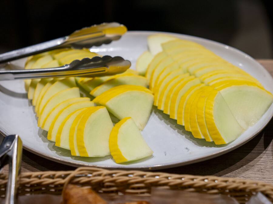 Ein Teller mit geschnittenem, gelb-grünem Obst, vermutlich Melone, dazu eine Zange.