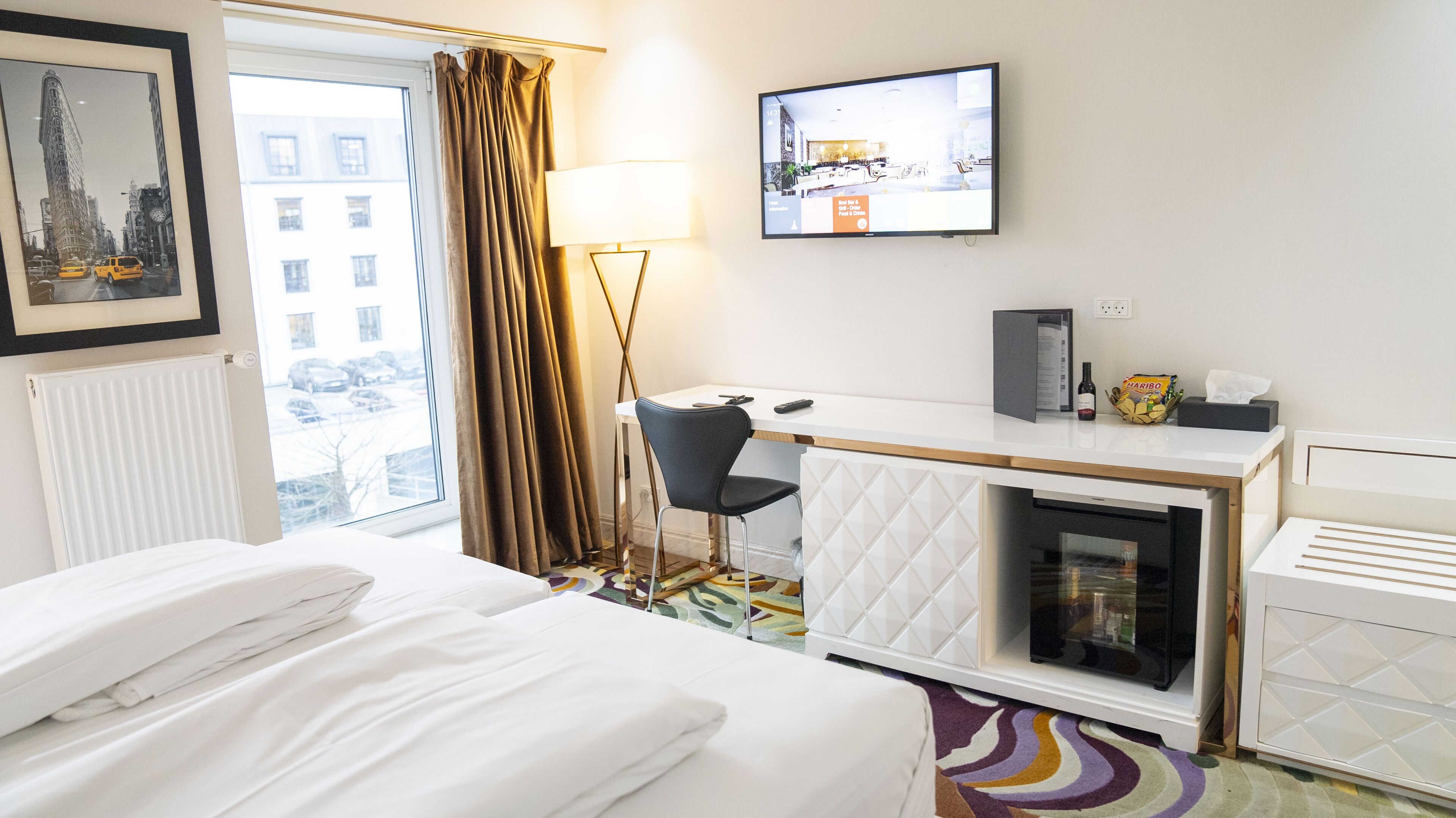 Een hotelkamer met een bed, bureau, stoel, televisie en uitzicht op de stad.